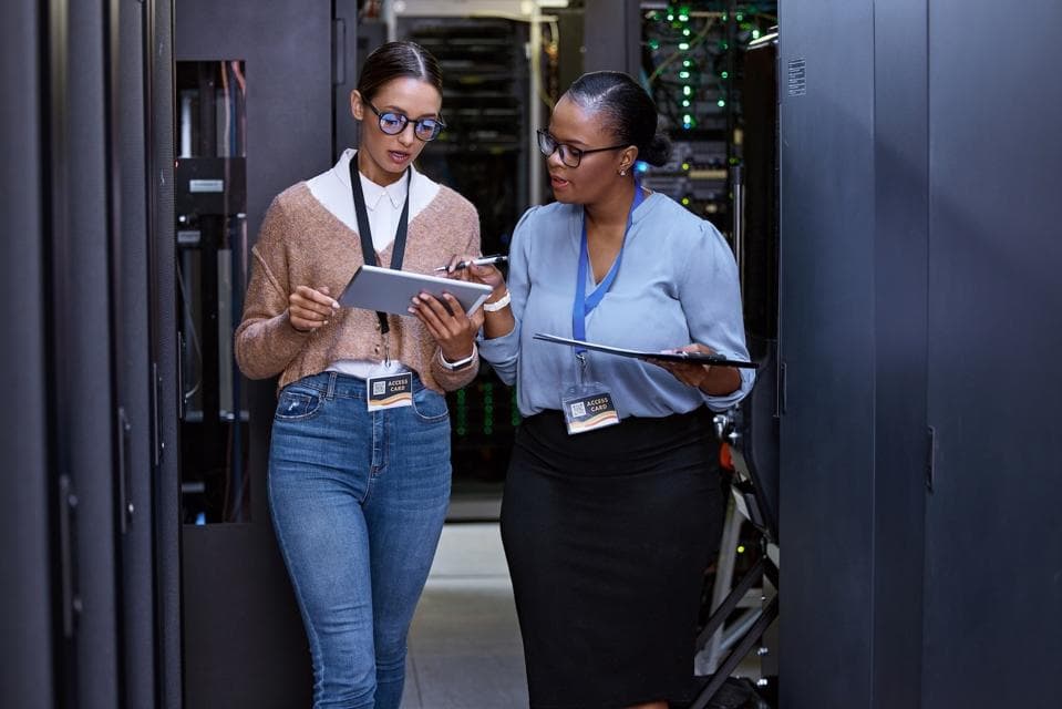 Two professionals with access badges reviewing secure infrastructure together in a server room.